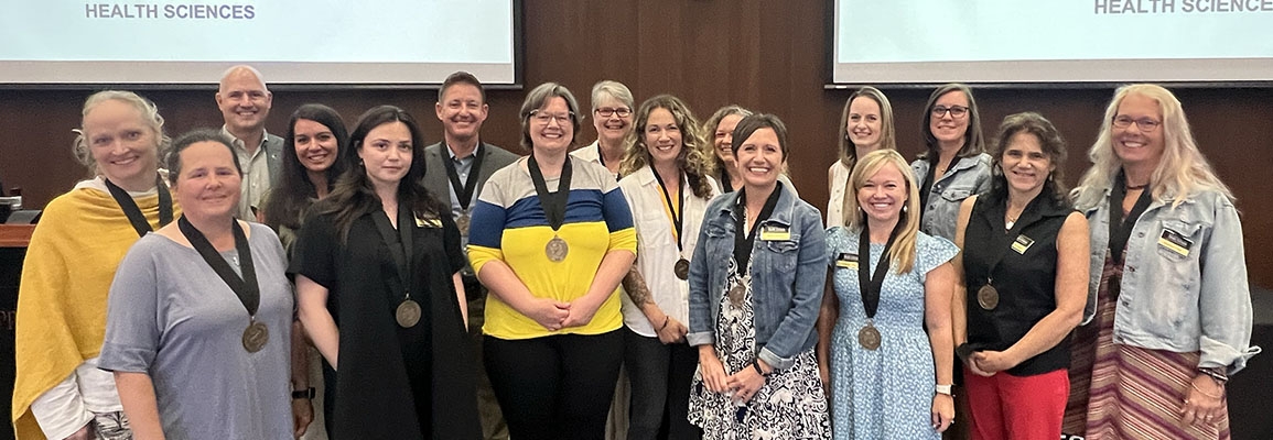 Group of people with medals around their necks stand in a group representing the college's award recipients for fall 2024 