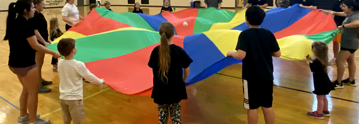 Group of kids and instructors hold brightly colored parachute to play the parachute game 