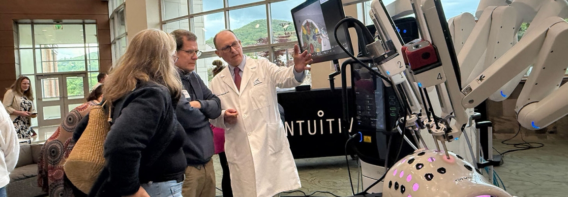 Man in white coat points to robotic arm while others look on 