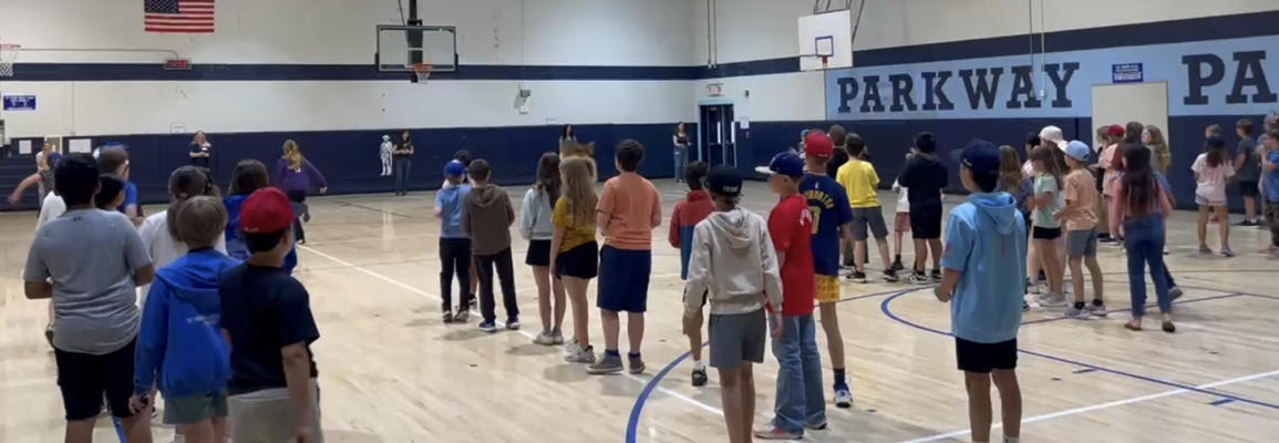 Large group of middle school students stand inside a school gymnasium 