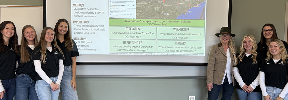 Two groups of women stand clustered around the end of a slide inside a classroom 