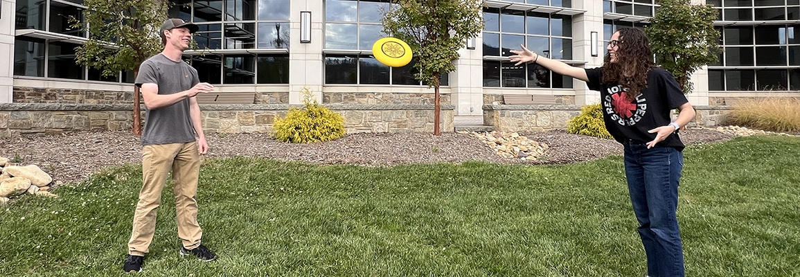 Two students play frisbee in front of Levine Hall. 