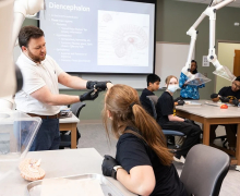 Students from Catawba County learn about brain anatomy under the instruction of Killian Wustrow, senior lecturer in App State’s Department of Kinesiology, far left, as part of a June 10 Camp Med session at the Levine Hall of Health Sciences on App State’s Boone campus. Camp Med at App State introduces students in grades 8–12 to health careers through experiential learning and exploration. The free summer program is offered by App State’s Appalachian Institute for Health and Wellness in partnership with Wake Forest University School of Medicine’s Northwest Area Health Education Center. Photo by Chase Reynolds Man with a beard in a scientific lab setting holds an object that younger people are looking at
