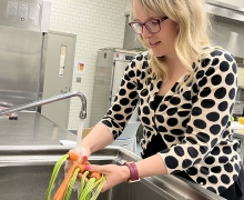 Woman wearing a polka dotted sweater washes carrots in an industrial sink.