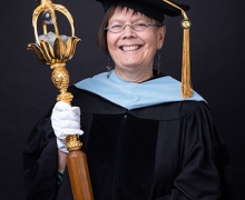 Person wearing regalia and holding a large wooden staff