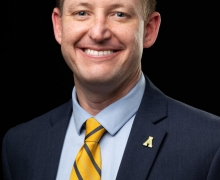 Man wearing a yellow tie and blazer smiles 