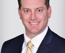 Man wearing a yellow tie and blue blazer smiles in a posed photo 