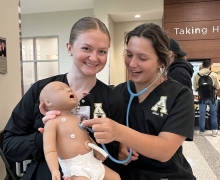 Students wearing scrubs hold a robotic baby simulation device 