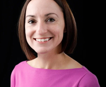Women in a magenta shirt has dark brown hair and smiles 