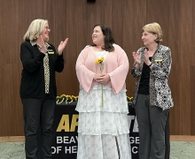 Student stands between two faculty members as they applaud