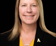 Image of a woman wearing gold shirt and black blazer