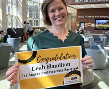 Woman smiles and holds a sign that says Inaugural Beaver Professor 