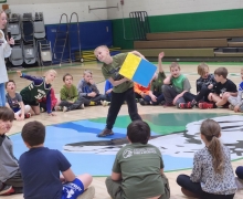 Student grabs a color block to roll it while other kids sit in a circle on the gym floor in Blowing Rock School