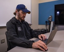 Person with a beard sits at a computer and is wearing a Medical Reserve Corps jacket