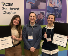 Two women hold certificates with a man standing between them and a banner behind them that reads SEACSM conference