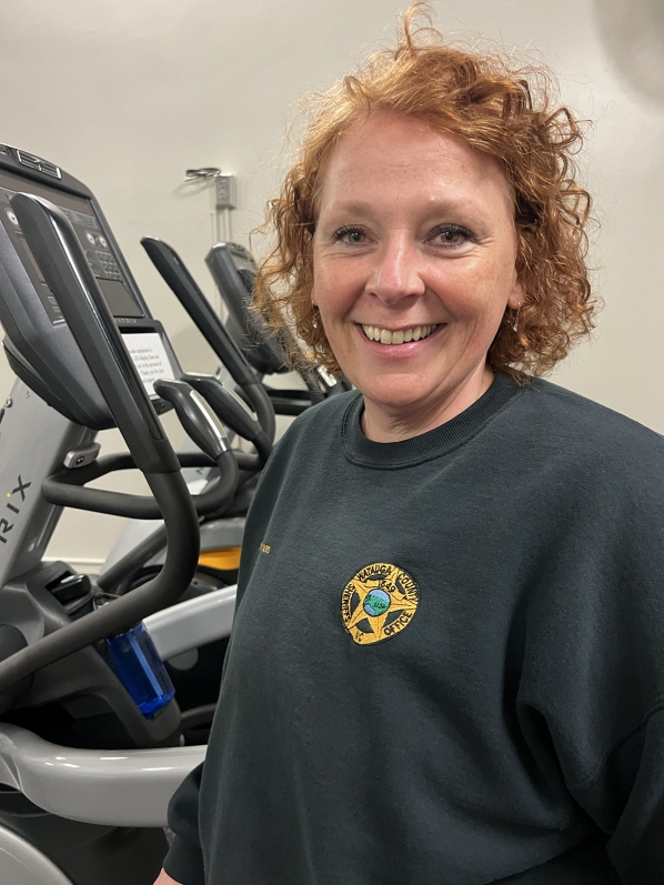 Woman smiles as she stands next to an elliptical machine 