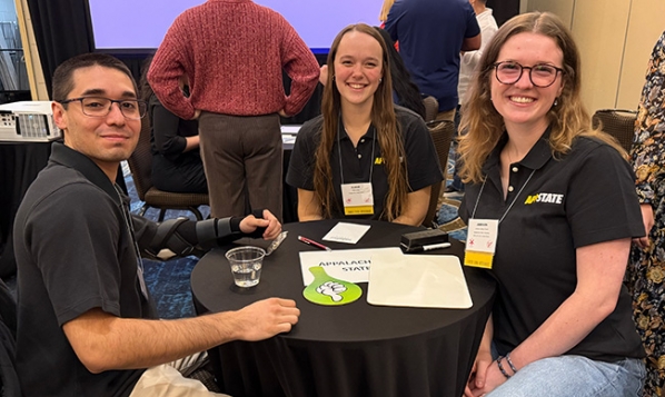 Three students wearing App State shirts sit around a table together 
