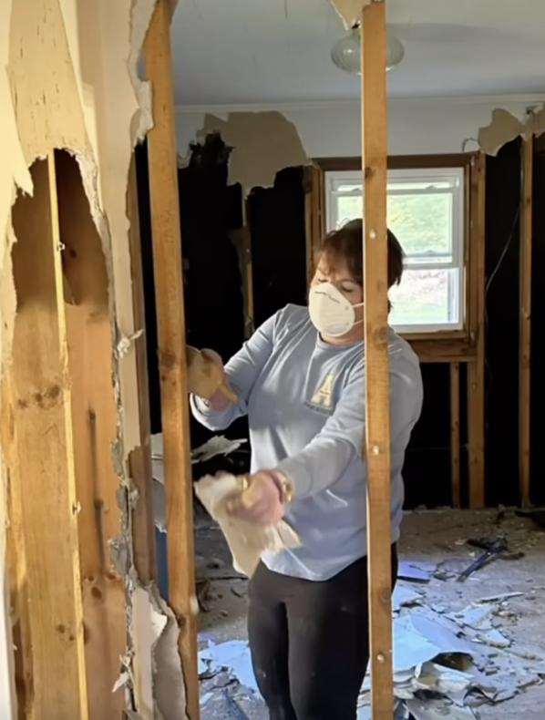 Woman wearing a mask helps remove insulation from a home. 