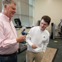 Older man grips a device in his right hand while a student looks on 