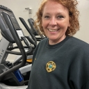 Woman smiles as she stands next to an elliptical machine 