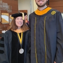 Woman and man wearing black and gold mortarboards stand next to each other 