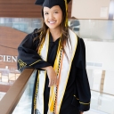 Graduate wears cap and gown and stands in lobby that says Health Sciences