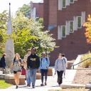 Group of students (one wearing an App State Football hoodie) walk toward the camera with a building behind them on the App State Boone campus.