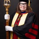 Woman wearing graduation regalia and holding a large staff