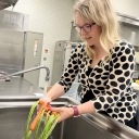 Woman wearing a polka dotted sweater washes carrots in an industrial sink.