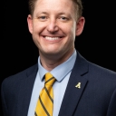 Man wearing a yellow tie and blazer smiles