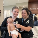 Students wearing scrubs hold a robotic baby simulation device