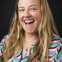 Woman with long, blonde hair wearing a brightly colored patterned shirt smiles with an animated grin 