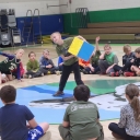 Student grabs a color block to roll it while other kids sit in a circle on the gym floor in Blowing Rock School