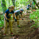 Group of people using rakes and other tools clear a trail in a natural trail area.