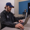 Person with a beard sits at a computer and is wearing a Medical Reserve Corps jacket