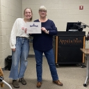 Two women are standing next to each other and are smiling; one is holding a certificate. 