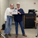 Two women are standing next to each other and are smiling; one is holding a certificate.