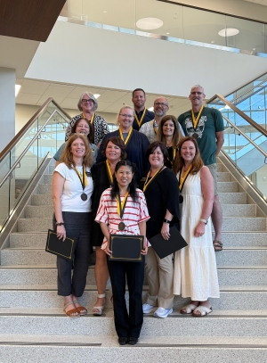 Group of 12 people stand in a large indoor atrium area while wearing medals and smiles