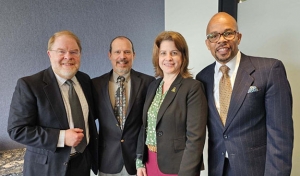 Group of four people in business attire stand next to each other smiling 