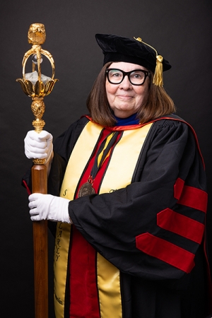 Woman wearing graduation regalia and holding a large staff