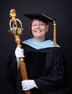 Person wearing regalia and holding a large wooden staff