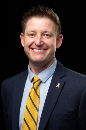 Man wearing a yellow tie and blazer smiles 