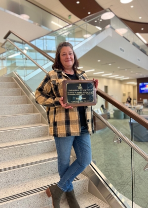 Woman stands on steps holding an award plaque