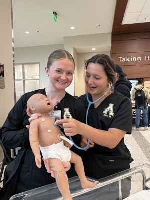Students wearing scrubs hold a robotic baby simulation device 