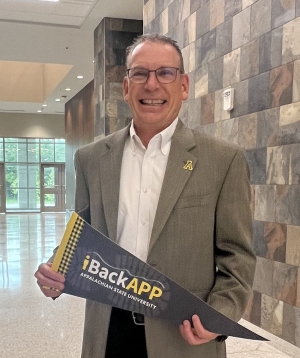Man wearing a blazer smiles as he stands inside the lobby area of a building