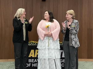 Student stands between two faculty members as they applaud