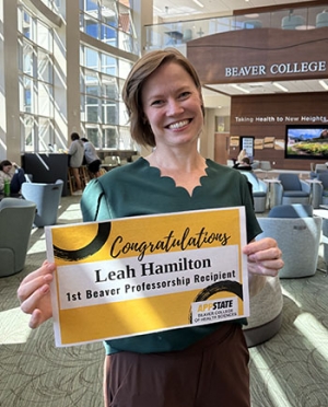 Woman smiles and holds a sign that says Inaugural Beaver Professor