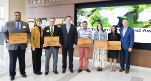 Group of people standing shoulder to shoulder, several are holding cutting boards with their names on them. 