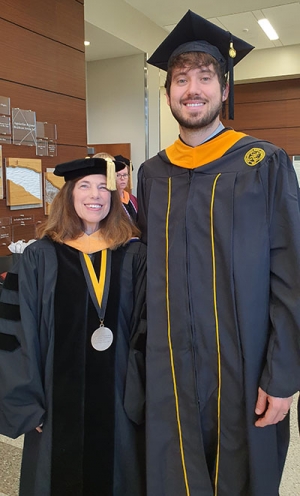 Woman and man wearing black and gold mortarboards stand next to each other 