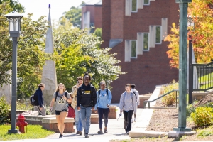 Group of students (one wearing an App State Football hoodie) walk toward the camera with a building behind them on the App State Boone campus.
